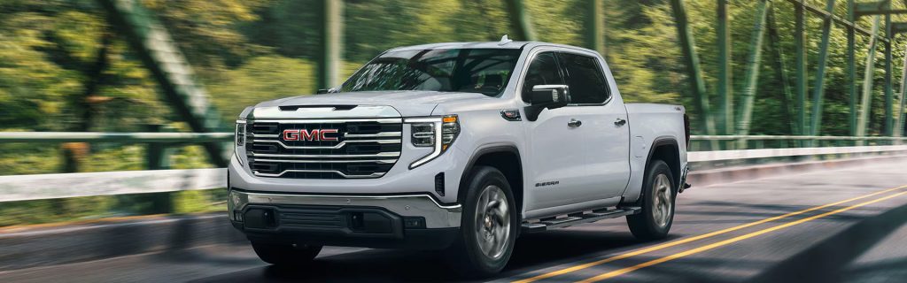 2026 GMC Sierra 1500 driving on a scenic road with bold grille and LED headlights